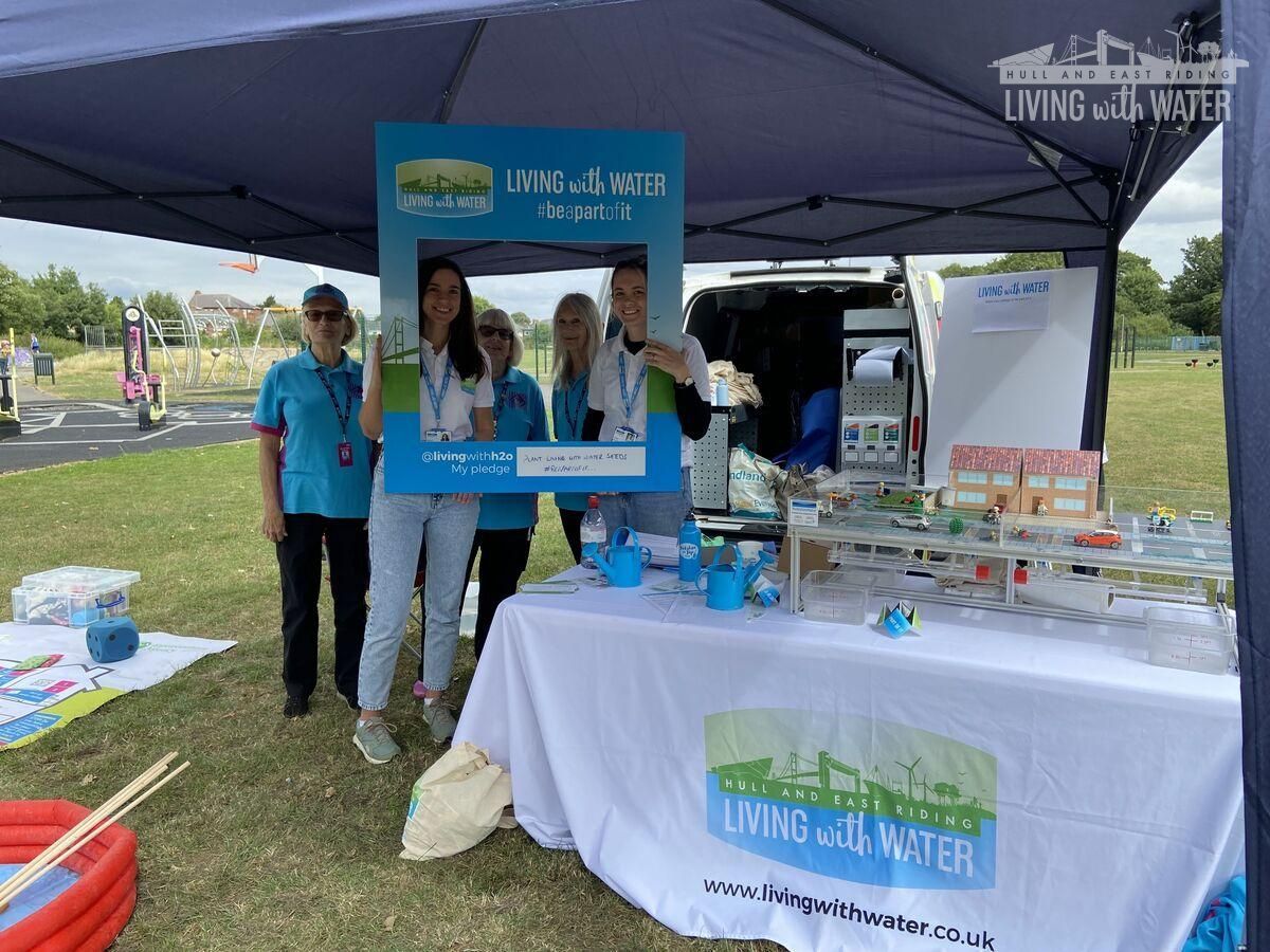 A photo of the living with water team at a convention, stood behind a Living With Water branded table and photo frame