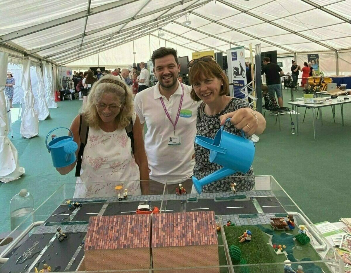 A photo of three people standing behind a table, putting water over two model houses
